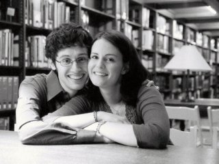 For their engagement photo session at the James J. Hill Reference Library in St. Paul, MN--Caleb Sancken has his left arm around Kristin Thomas' shoulder and the other arm on a wood table at which they're both sitting.  Kristin has her arms folded in front of her on the table surface.
